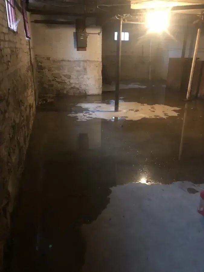 Floodwater across the floor of an old brick and stone basement, water damage restoration in Brookline, MA
