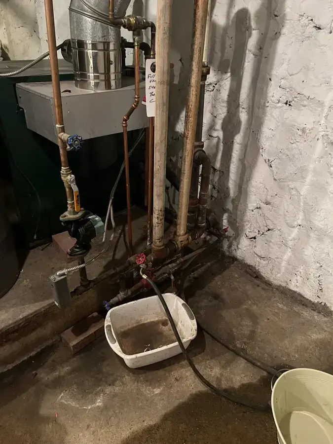 Old boiler piping in a basement corner with buckets catching drips, water damage restoration in Brookline, MA