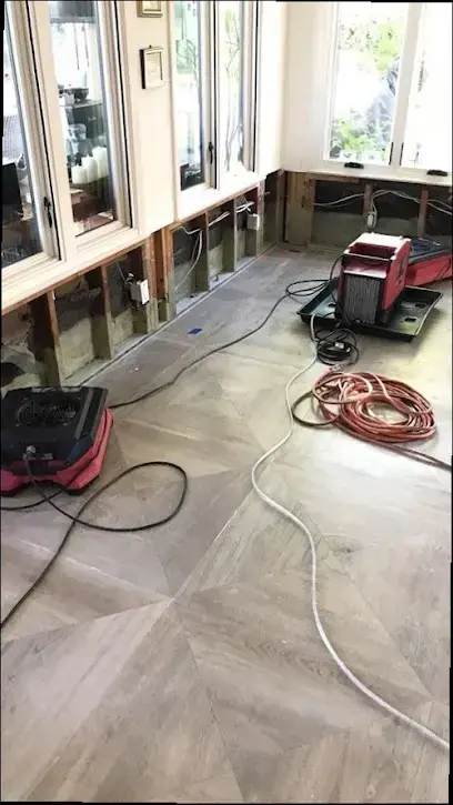 Red air movers running along a floor beside a wall cut open at the base during a Dedham dry out