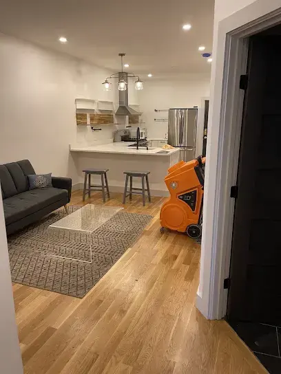 An orange dehumidifier running in a finished living room with hardwood floors while a Needham home is dried after water damage